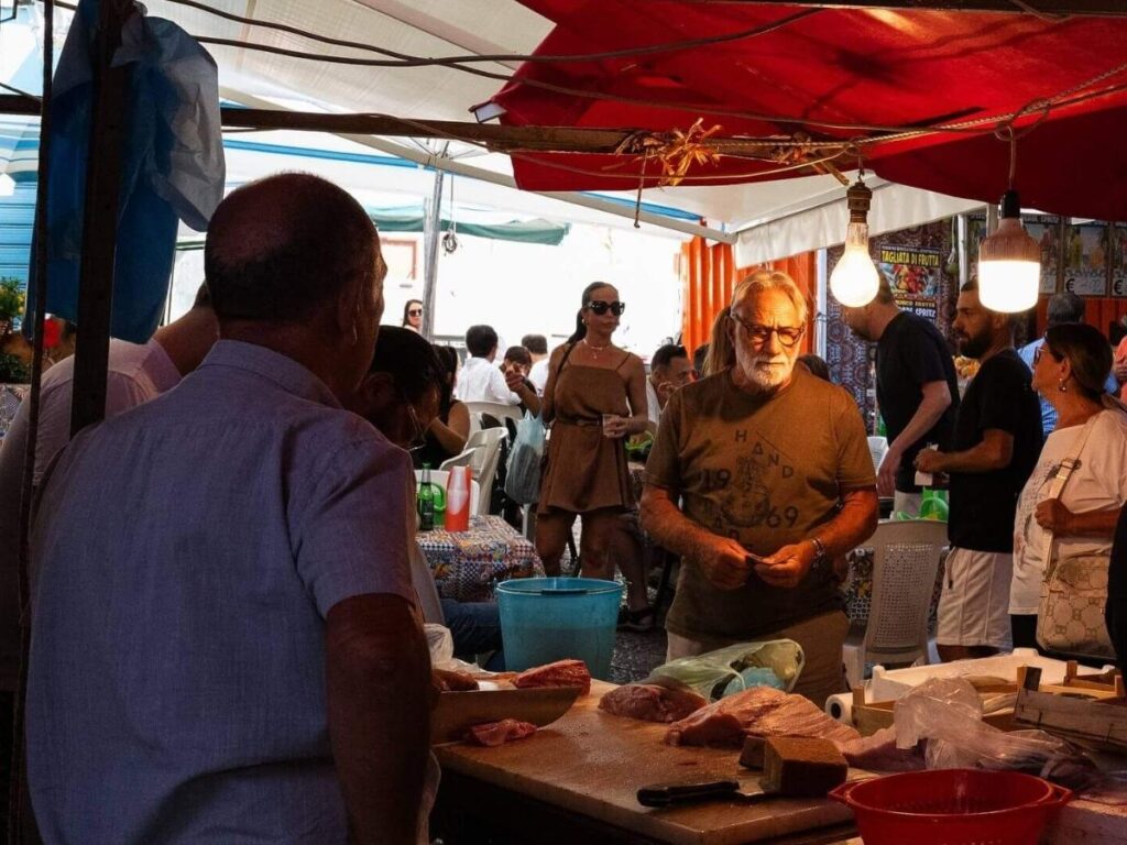 Locals shopping and eating at a colorful street-food stall in Ballarò Market, Palermo