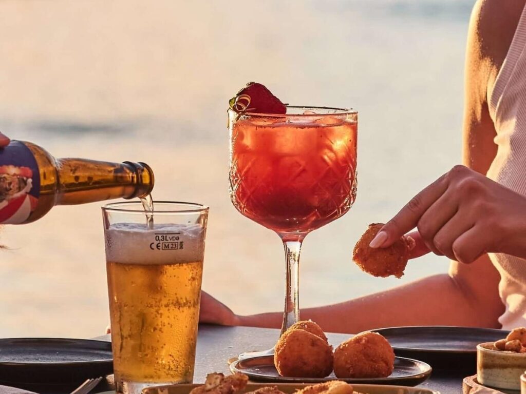Glass of Aperol spritz on a rooftop bar overlooking Palermo rooftops and Cathedral at sunset