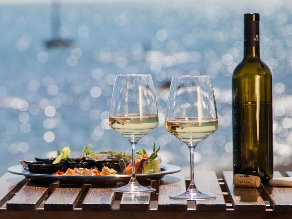 Glass of Pecorino white wine beside a plate of grilled fish and lemon, set on an outdoor table by the sea