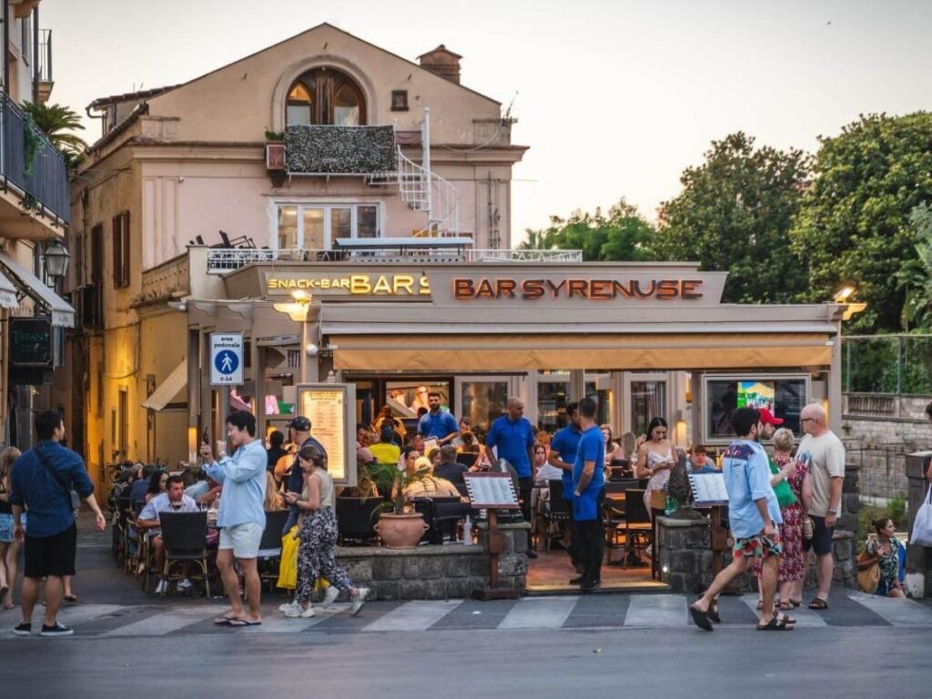 Morning light over Piazza Tasso in Sorrento with locals drinking espresso and scooters parked nearby.