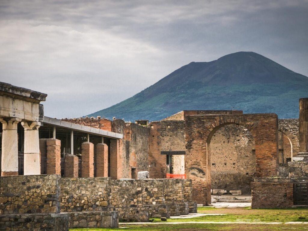 Stone street in Pompeii with Mount Vesuvius visible in the distance under a clear sky.