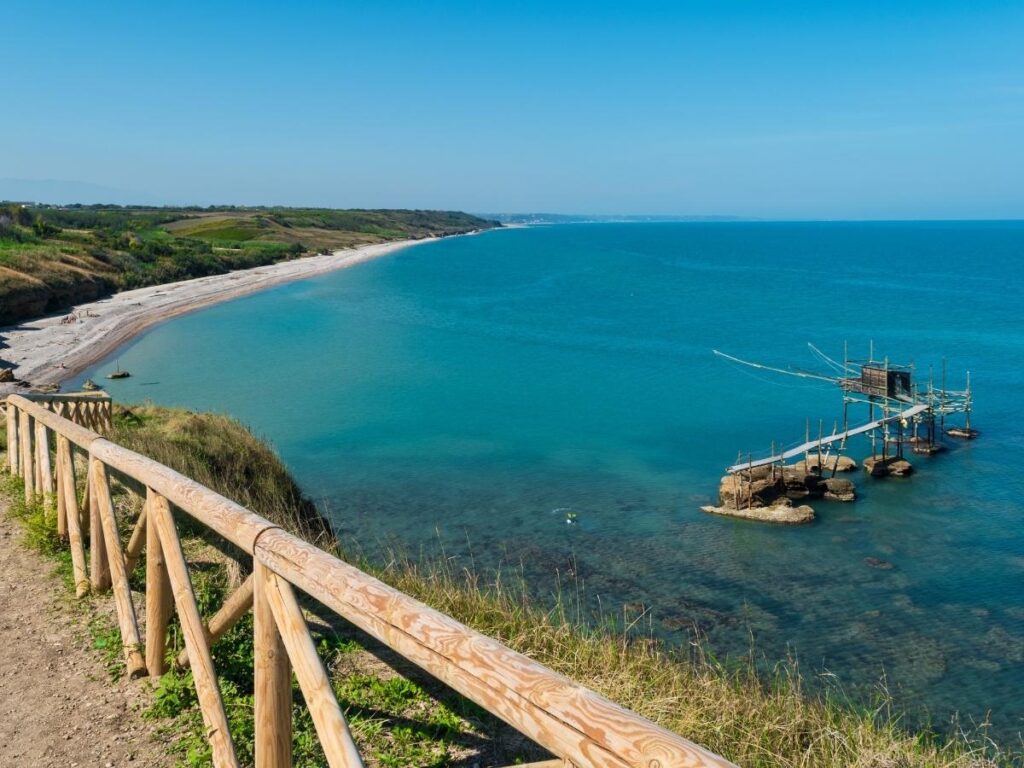 Rugged cliffs and clear blue coves in Punta Aderci nature reserve, a picnic blanket on a rocky outcrop.