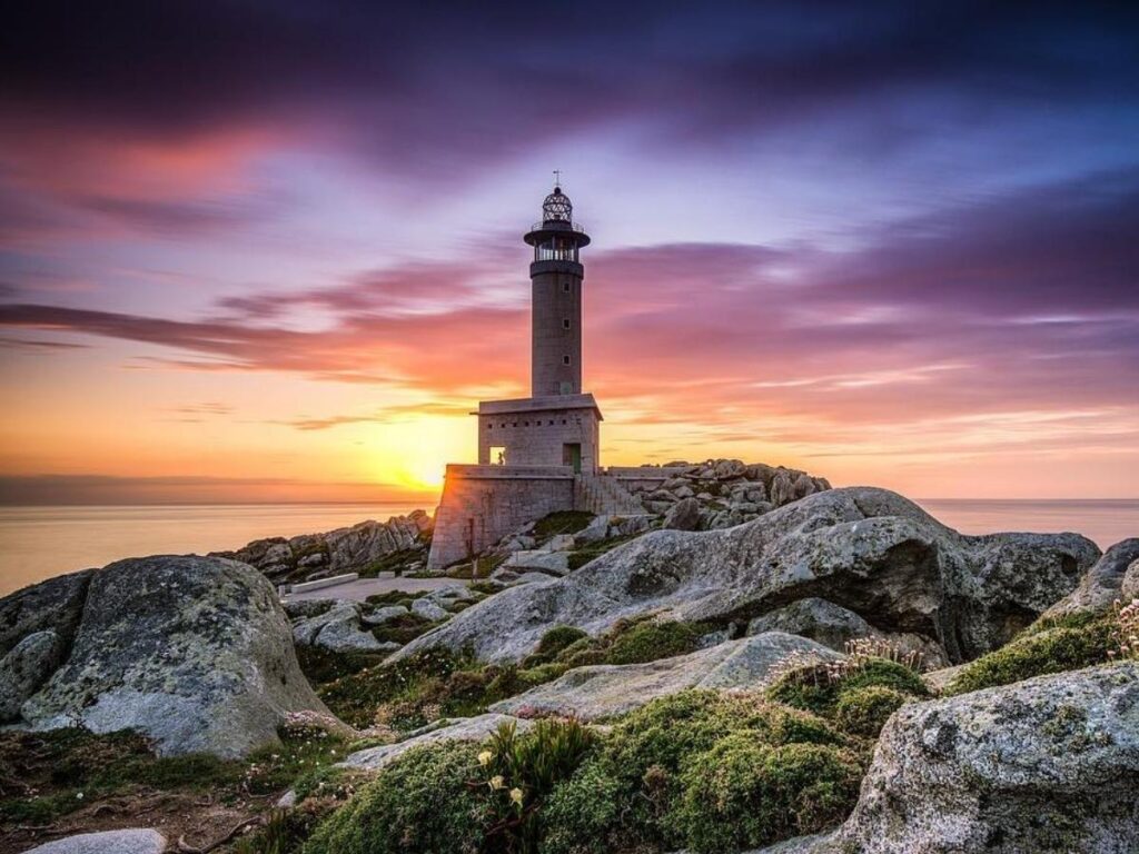 Red lighthouse at Punta Faro with wooden pier at sunset