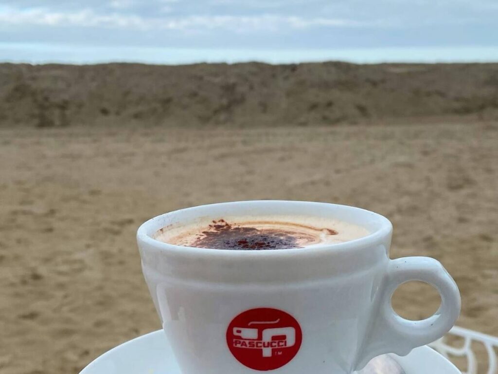 Woman sipping cappuccino barefoot on the sand at Riccione beach during early morning light