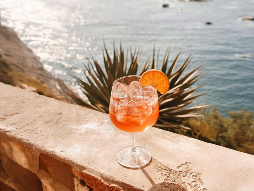 Glasses of Aperol spritz at a waterfront bar overlooking Riccione harbor at sunset