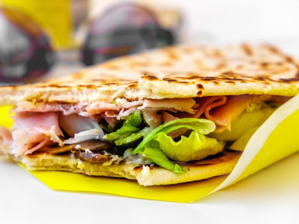 Local vendor preparing fresh piadina stuffed with prosciutto and cheese in Rimini.