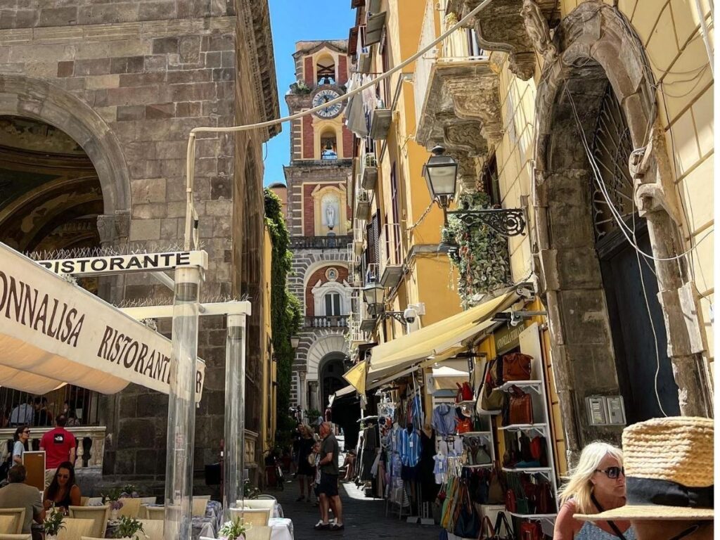 Narrow cobbled alley in Sorrento’s Old Town glowing with evening lights, cafés, and locals chatting outside.