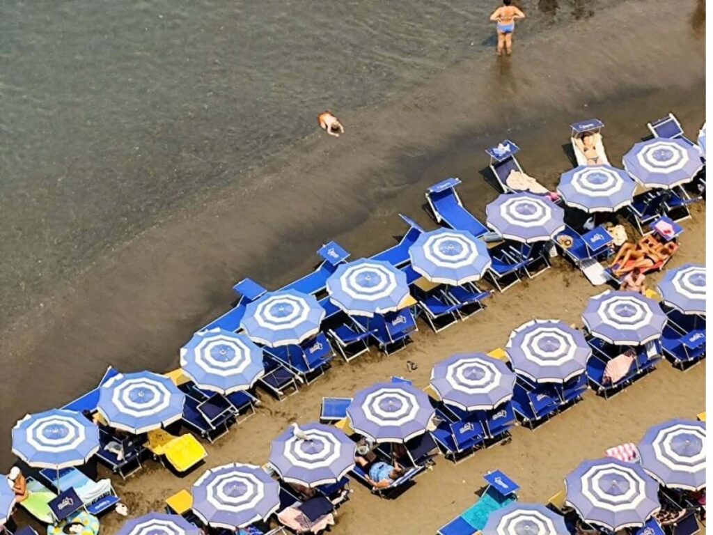 Colorful parasols and sun loungers lining a busy beach club in Sorrento during summer