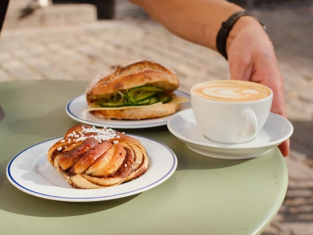 Cardamom bun on a plate beside a steaming cup of coffee, café table scene