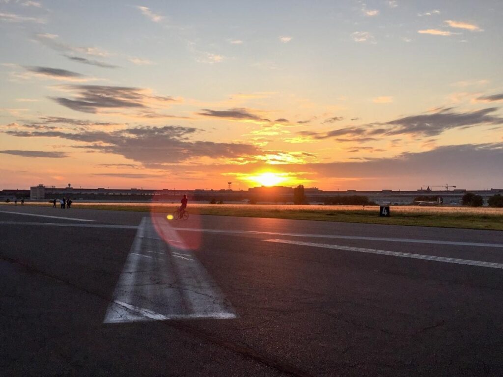 People cycling and flying kites across Tempelhofer Feld park at sunset in Berlin