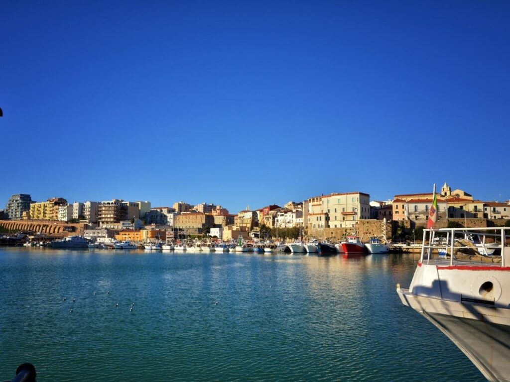 Locals enjoying aperitivo near Termoli harbor with fishing boats and sunset light over the water.