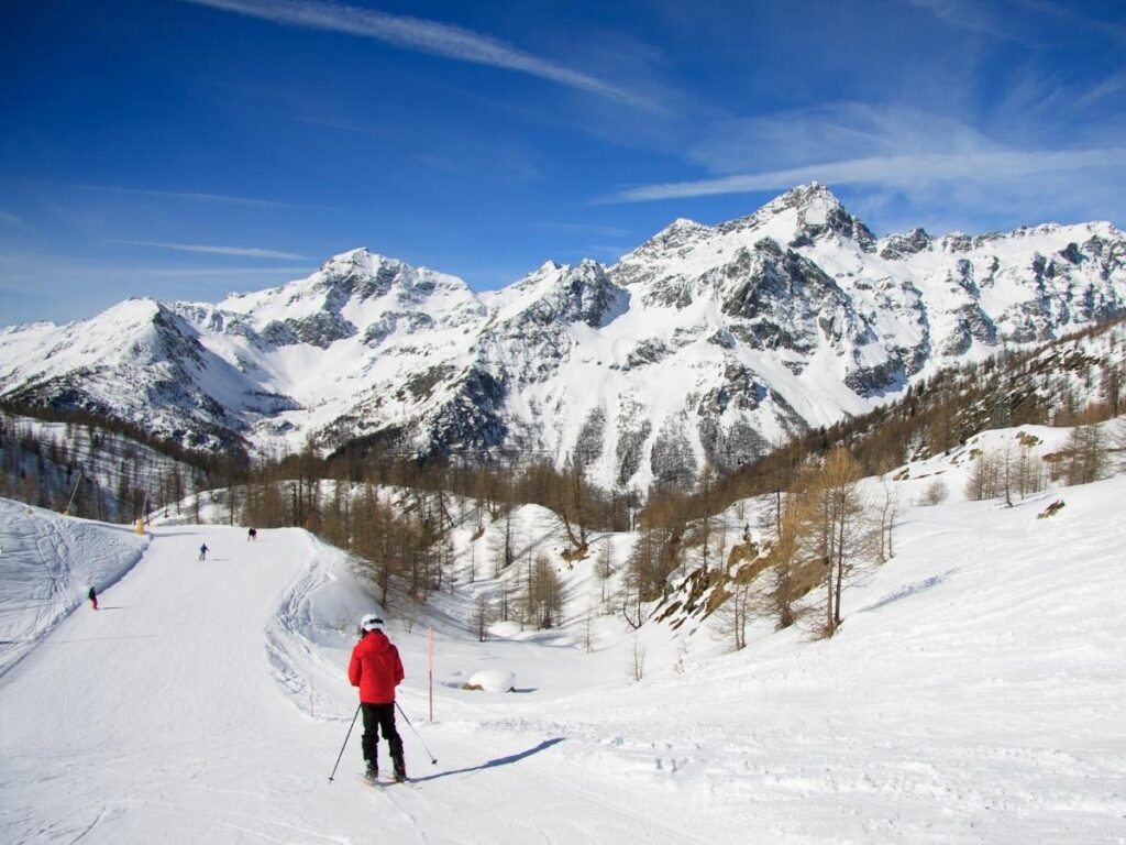 Skiers descending a snow-covered run near Courmayeur with chalets and pine trees lining the piste.