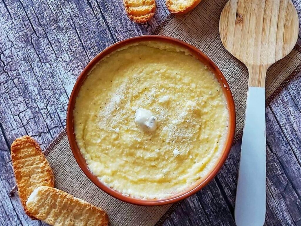Close-up of polenta concia topped with melted fontina cheese served in a rustic wooden dish.