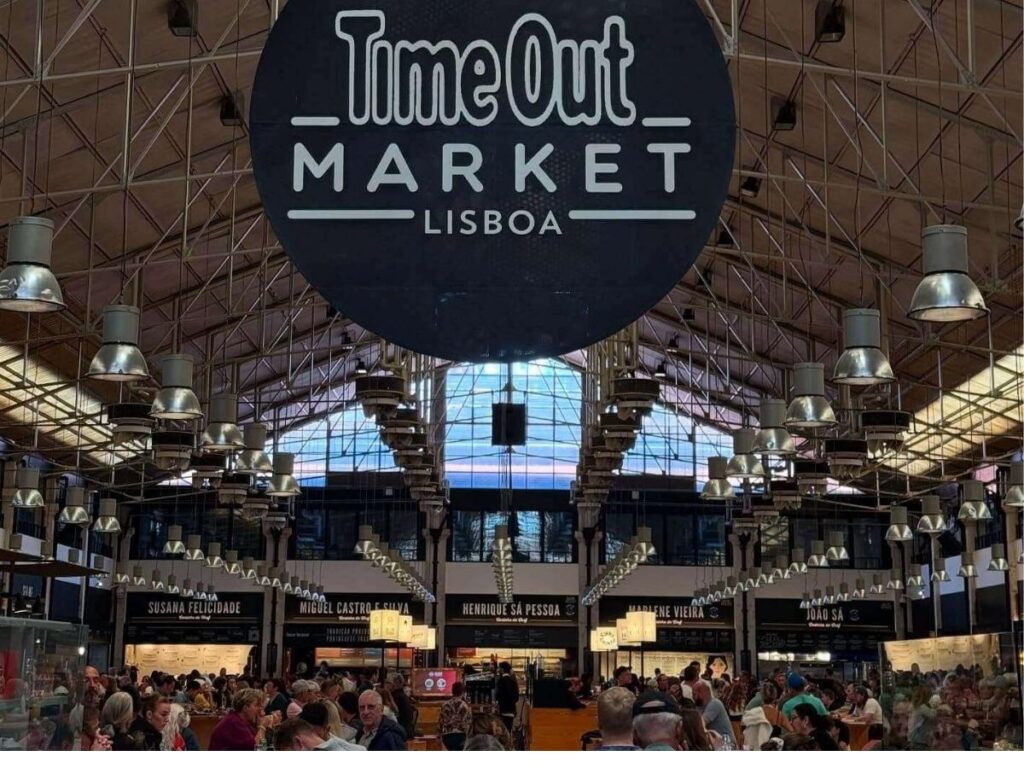 Busy stalls and communal tables inside Time Out Market Lisbon filled with people eating