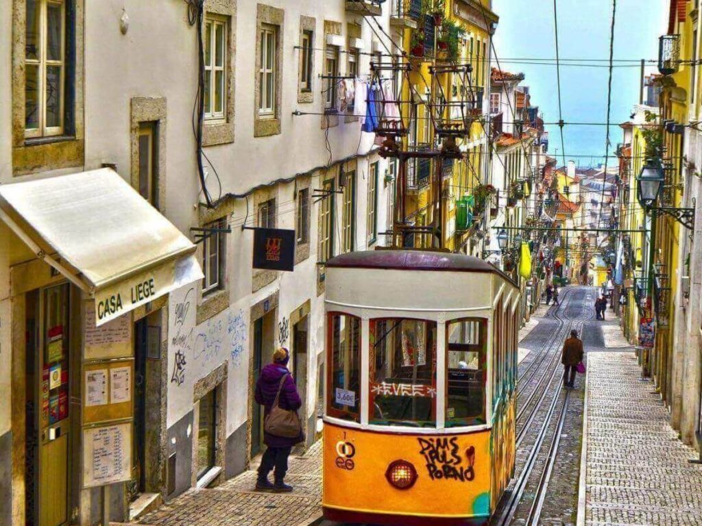 Yellow Tram 28 climbing a narrow, colorful street in Lisbon’s Bica neighbourhood