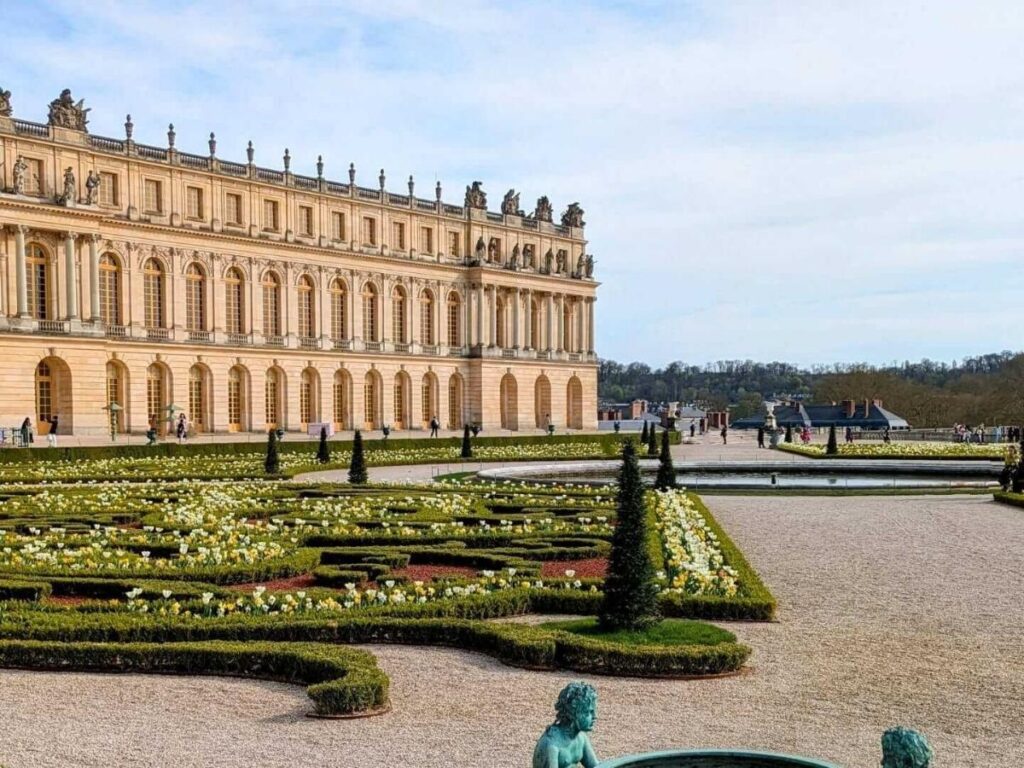 Visitors walking through the manicured gardens of the Palace of Versailles near Paris