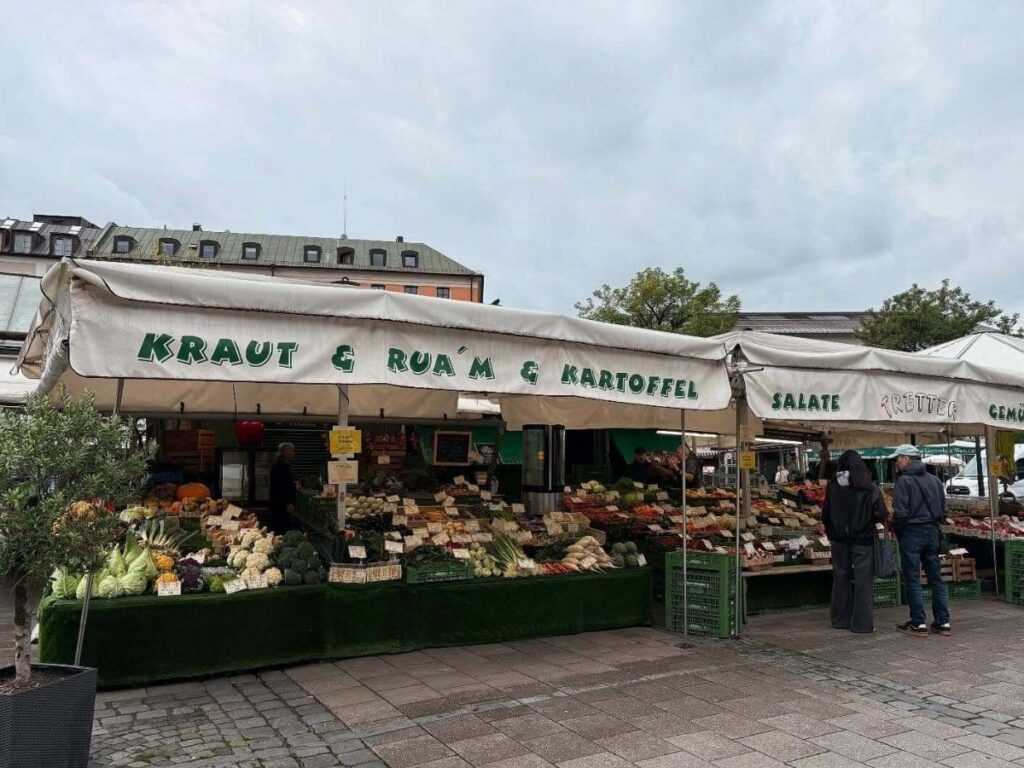 Colourful Viktualienmarkt food stalls and a baker holding a fresh pretzel.