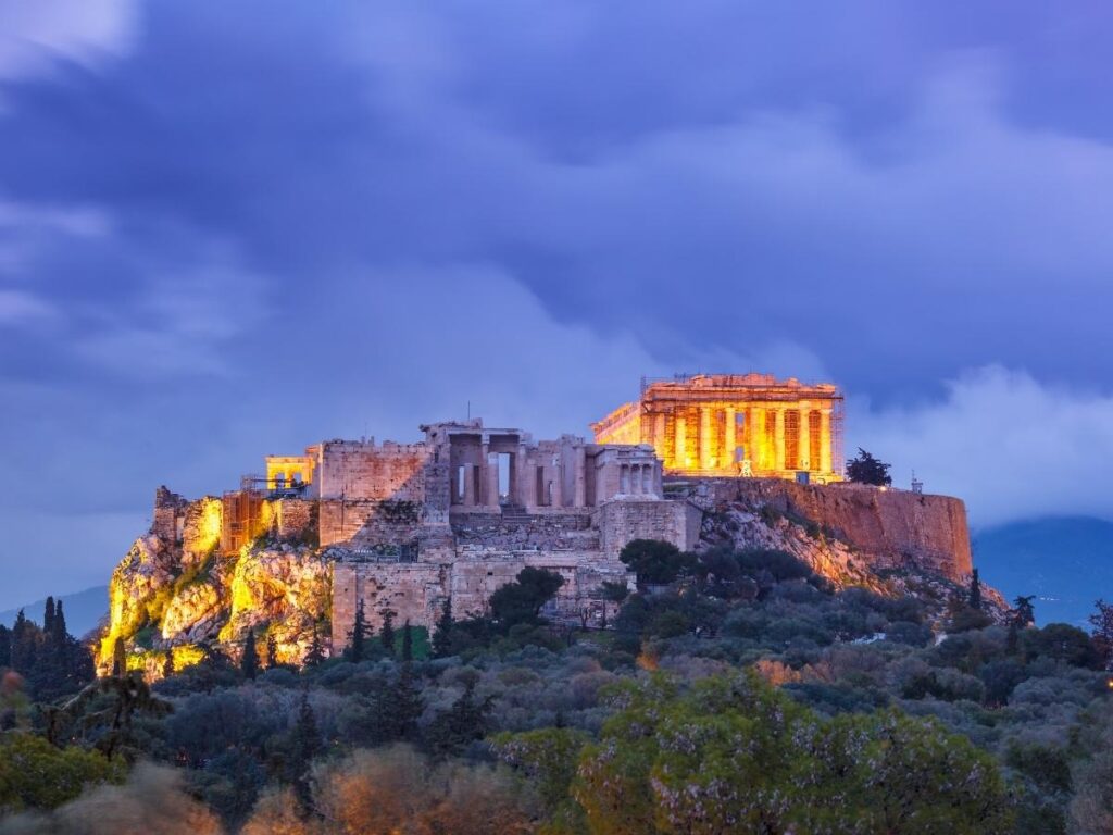 he illuminated Parthenon at night seen from a rooftop terrace, wine glass in the foreground