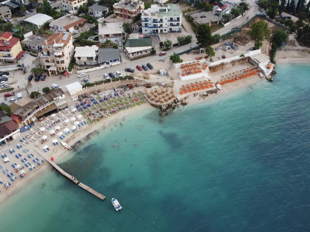 Crowded summer beach on the Albanian Riviera with umbrellas, swimmers and bright midday sun