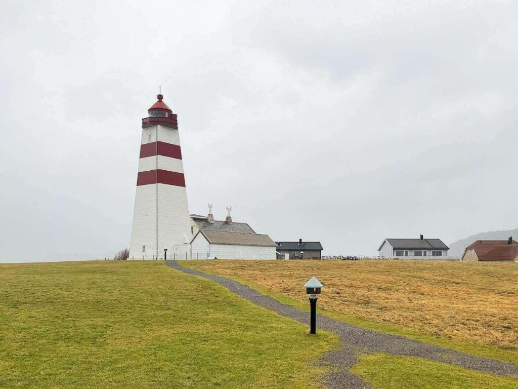 Alnes Lighthouse on Godøy at sunset with waves and coastal path