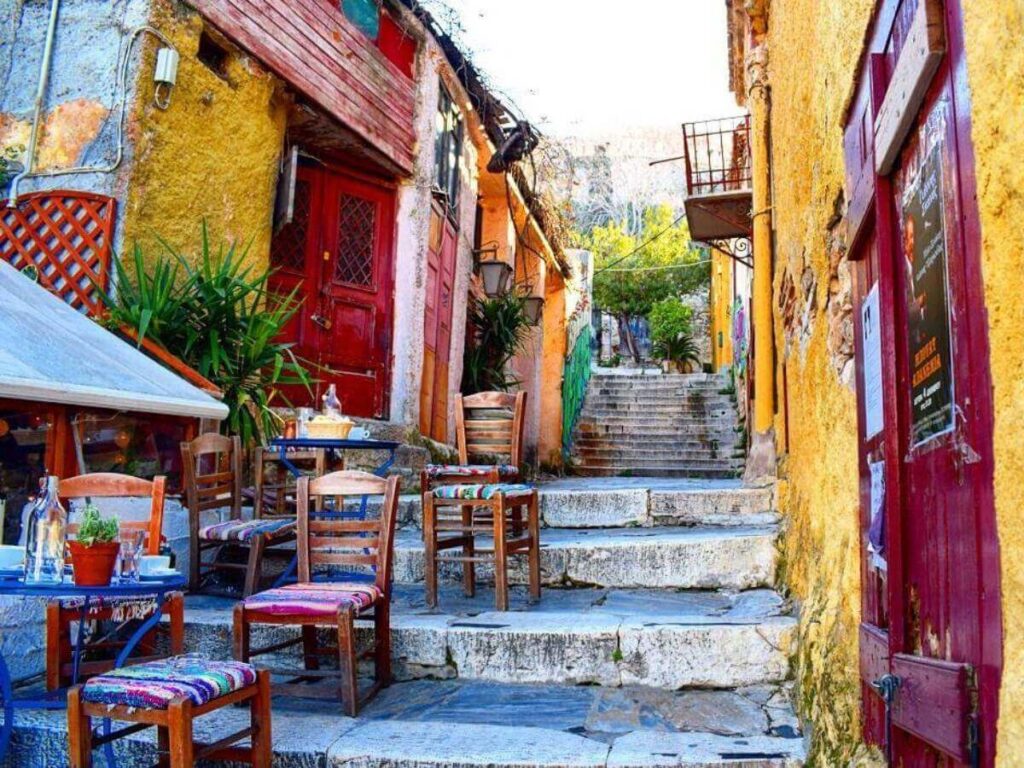Outdoor taverna table in Anafiotika with plates of Greek food, shaded by vines and stone walls nearby.