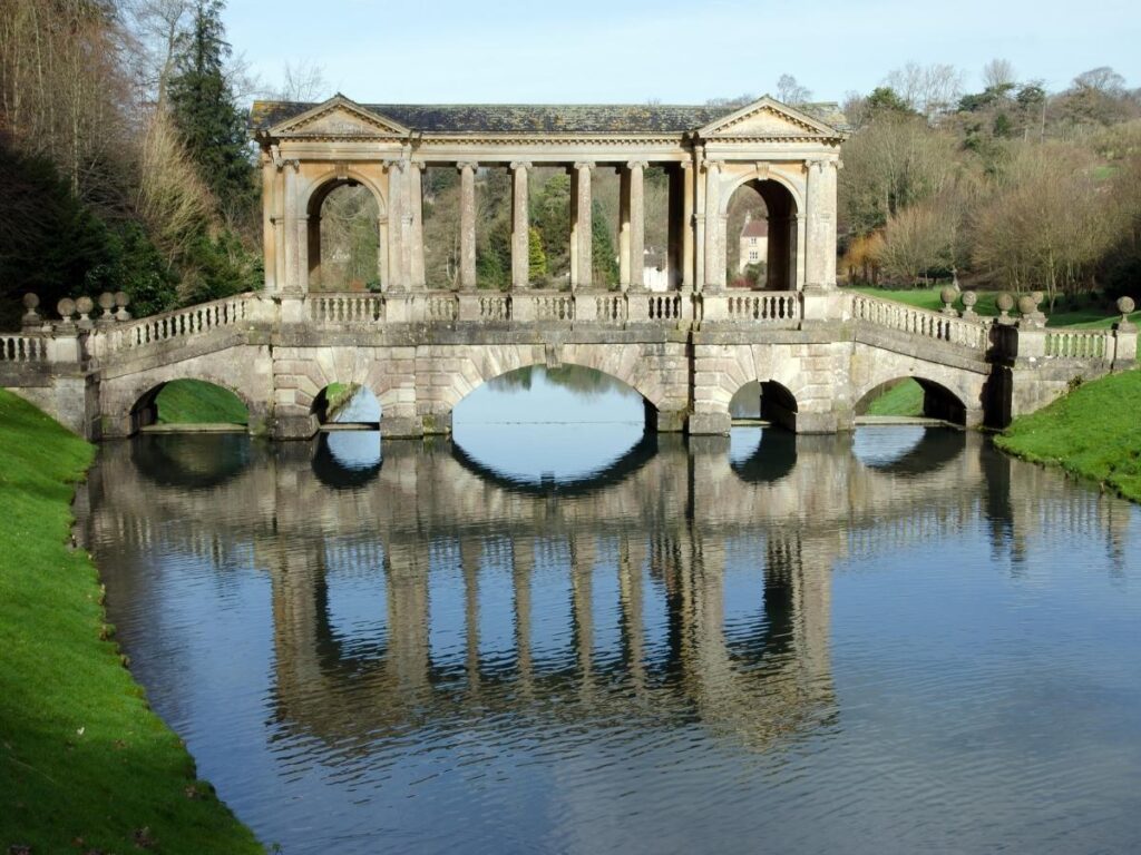 Palladian Bridge at Prior Park reflected in the still lake with trees and valley views