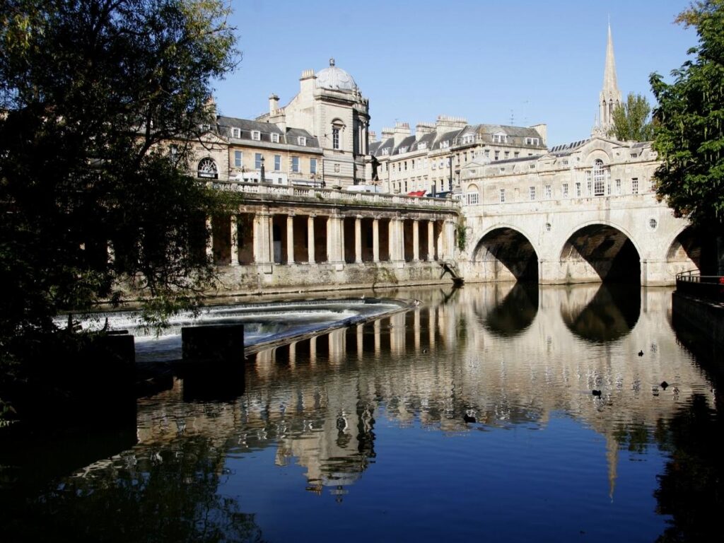 Evening view of Pulteney Weir with the water curving gently and warm lights reflecting on the river