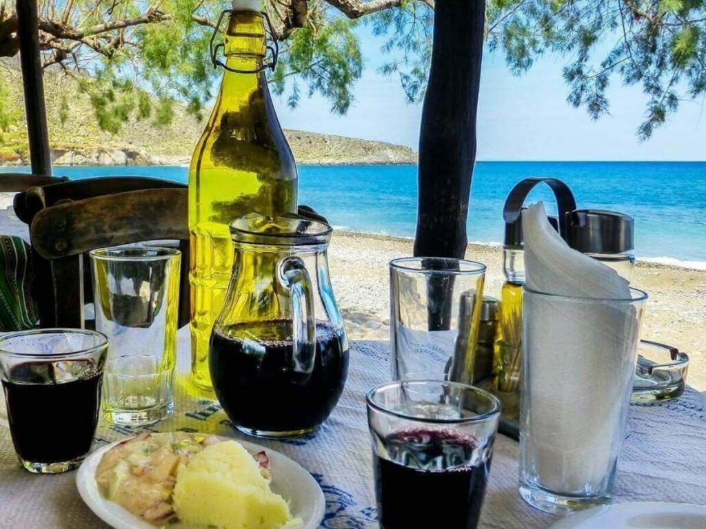 Seaside taverna table with grilled fish, salad, and a carafe of white wine by the water