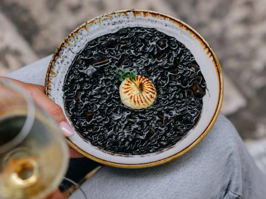 Close-up of black risotto with cuttlefish and lemon wedge on a rustic plate