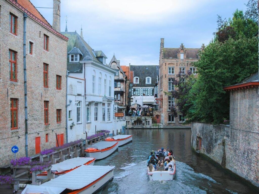 Tour boat passing under bridges on the canals of Bruges on a sunny afternoon