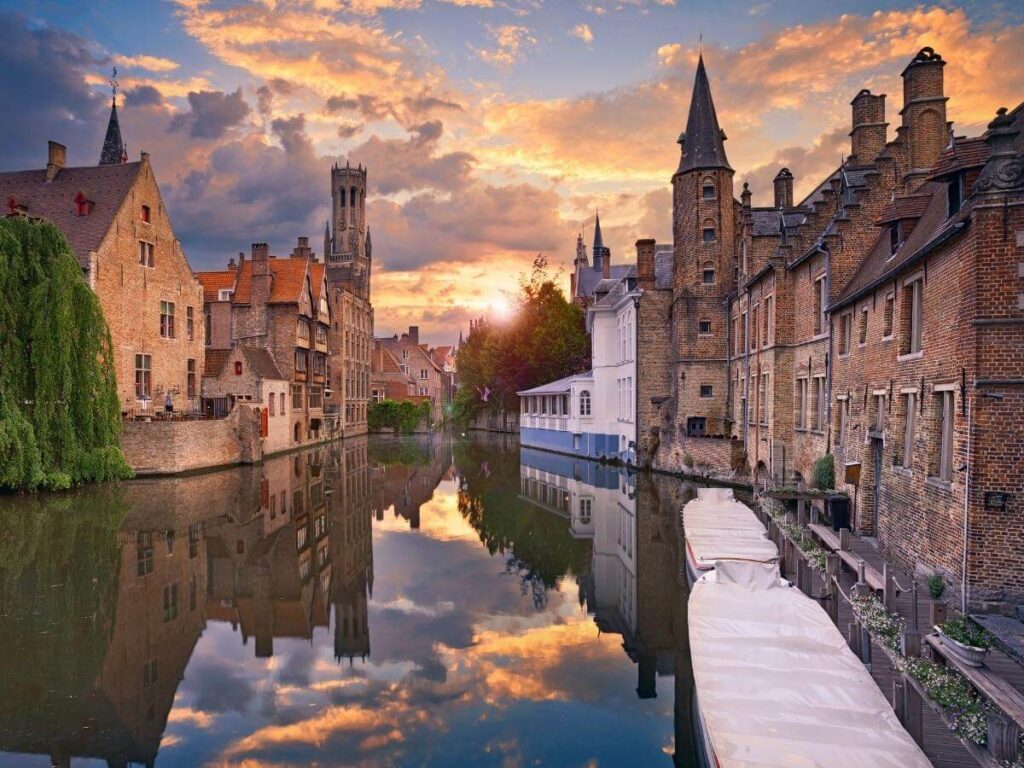 Soft sunrise light over a quiet Bruges canal with empty paths and reflections
