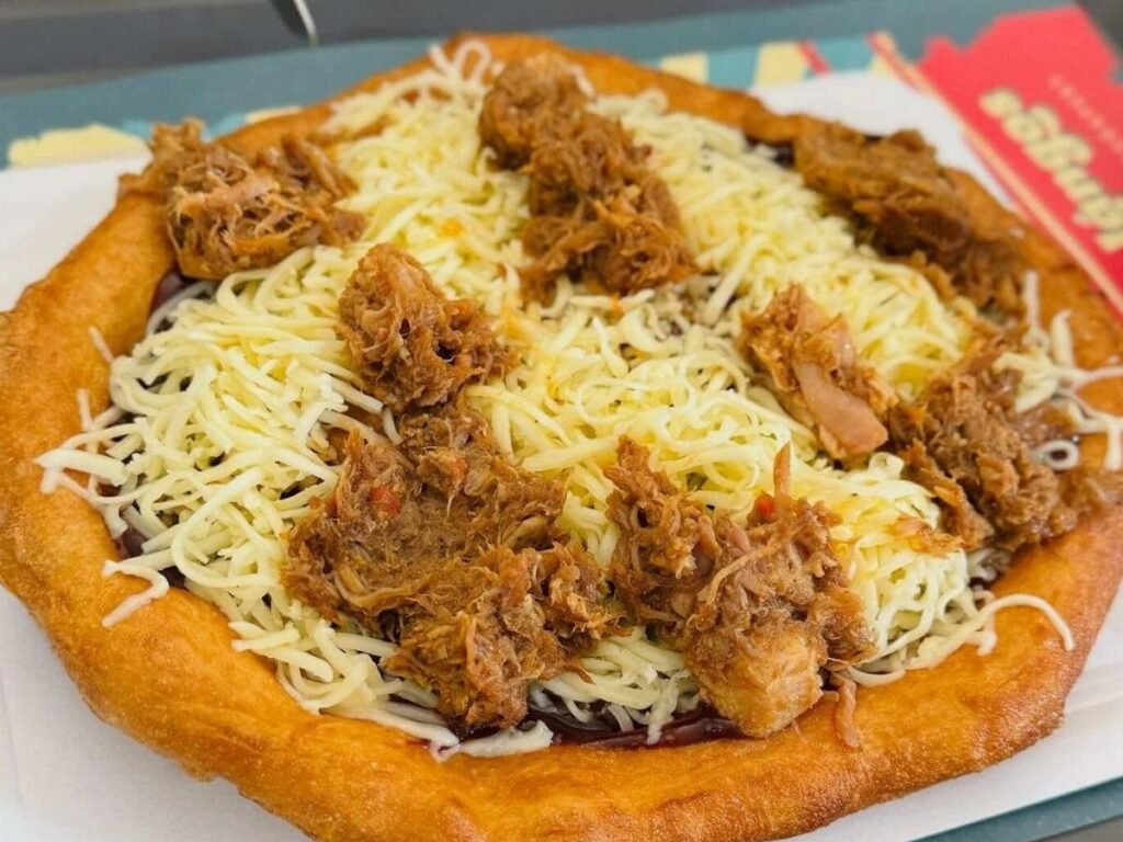 Fresh Hungarian lángos topped with sour cream and cheese served on a plate
