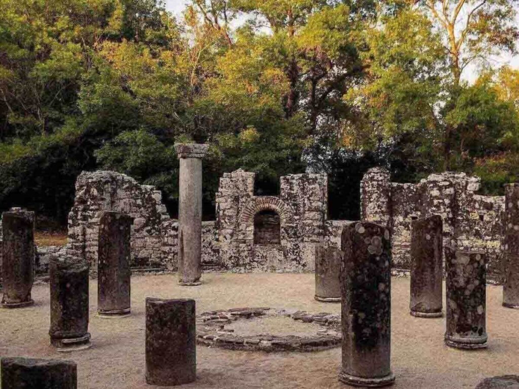 Ancient stone ruins of Butrint National Park with shaded paths and lagoon in the background