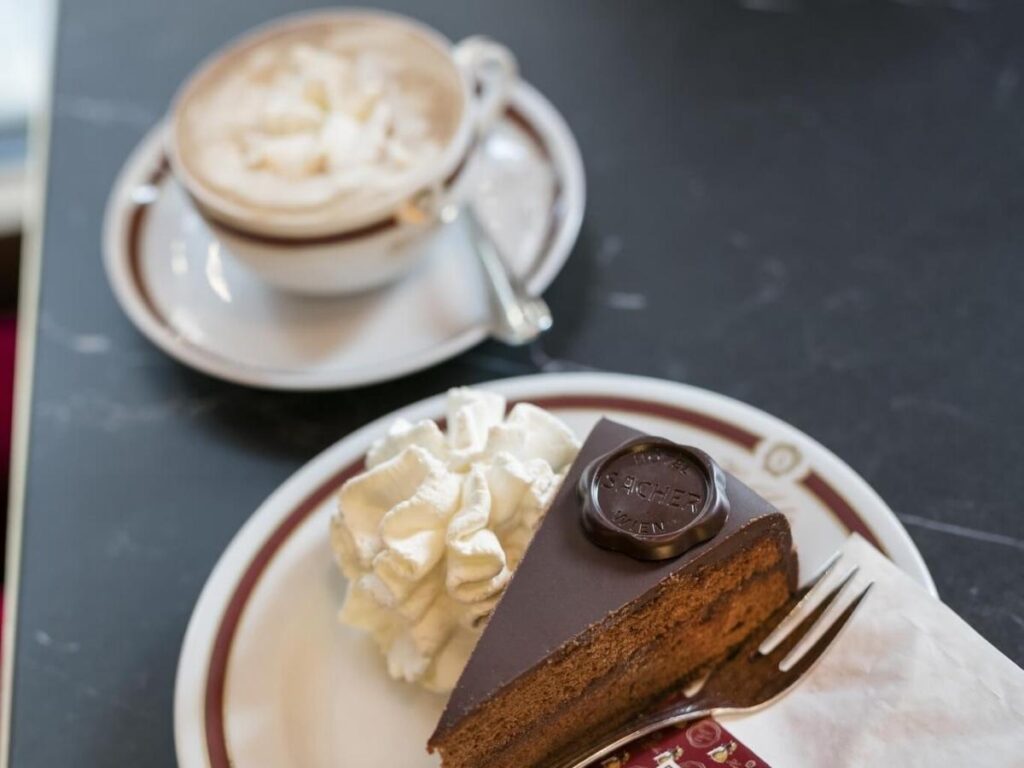 Viennese Melange and a slice of Sachertorte on a marble table inside Café Central