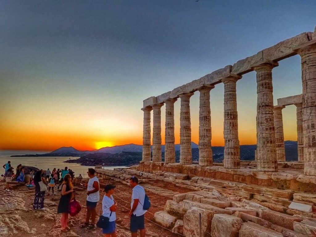 Temple of Poseidon silhouetted on the cliff at sunset, orange sky reflected on the sea