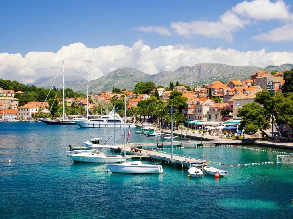 Small wooden boat cutting across the Adriatic with Cavtat’s red rooftops visible in the distance