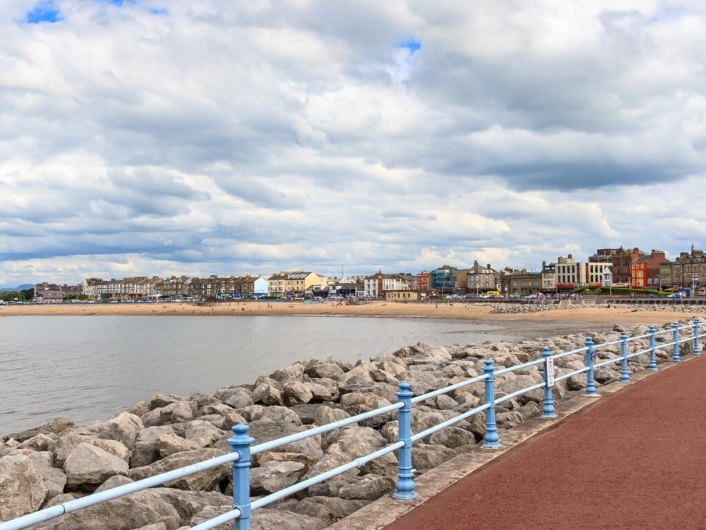 Early morning on the seafront promenade — empty tables, a lone cyclist and soft light on stone buildings.