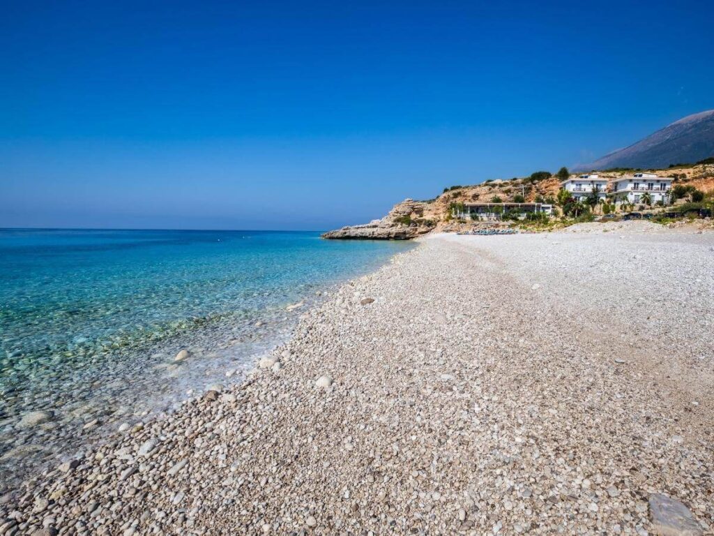 Early morning light over Dhërmi Beach with calm water and smooth pebbles