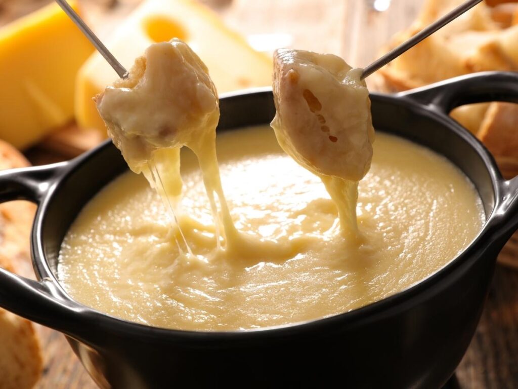 Traditional Swiss cheese fondue served with bread cubes on a wooden table