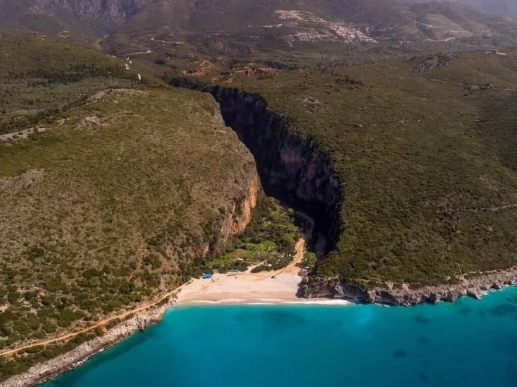 Rocky canyon path leading down to Gjipe Beach, with high cliffs and a small beach below