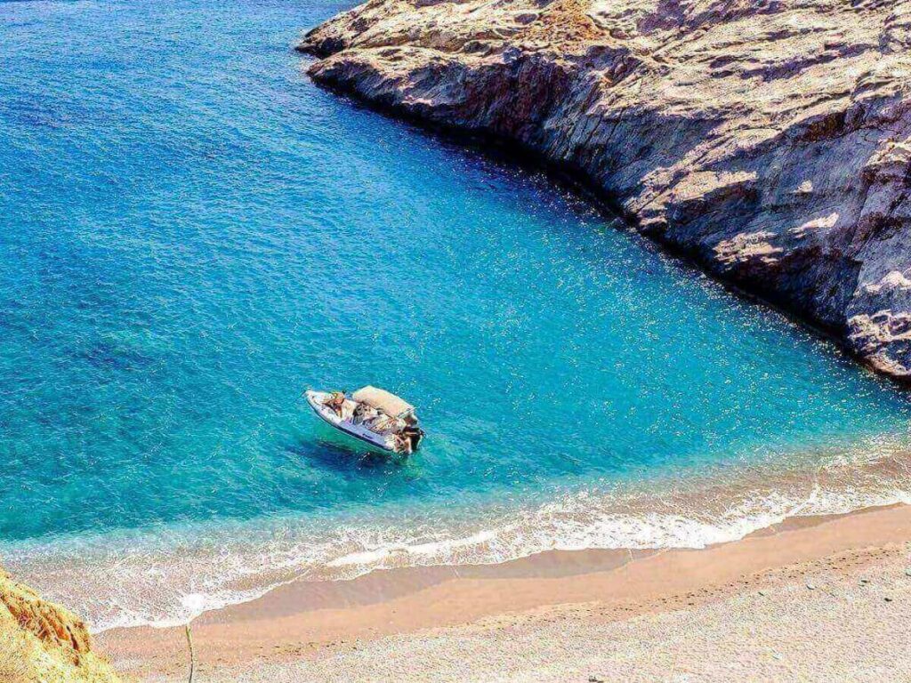 Small wooden boat arriving at Katergo beach, Folegandros, with cliffs and turquoise water