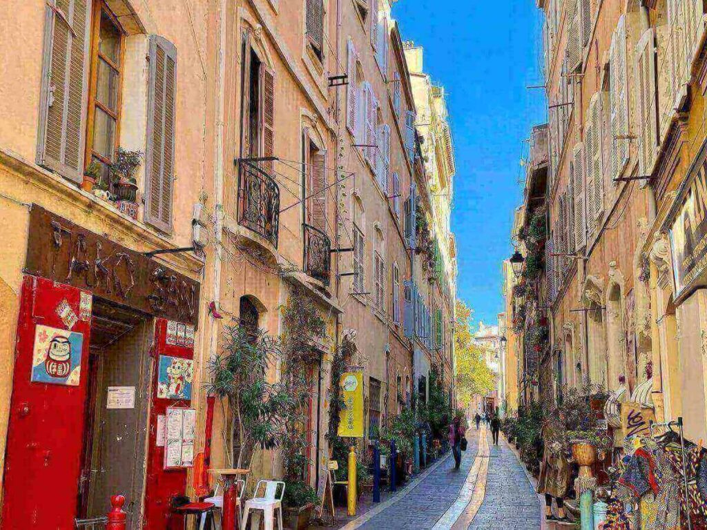 Narrow cobbled lane in Le Panier with pastel façades, street art and a small café terrace