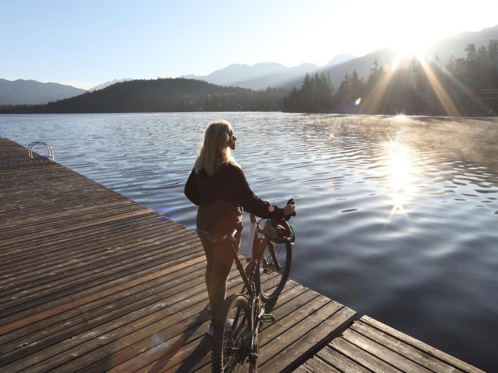 Cyclist on the shaded lakeside path circling Veliko Jezero, pine forest on one side and water on the other.