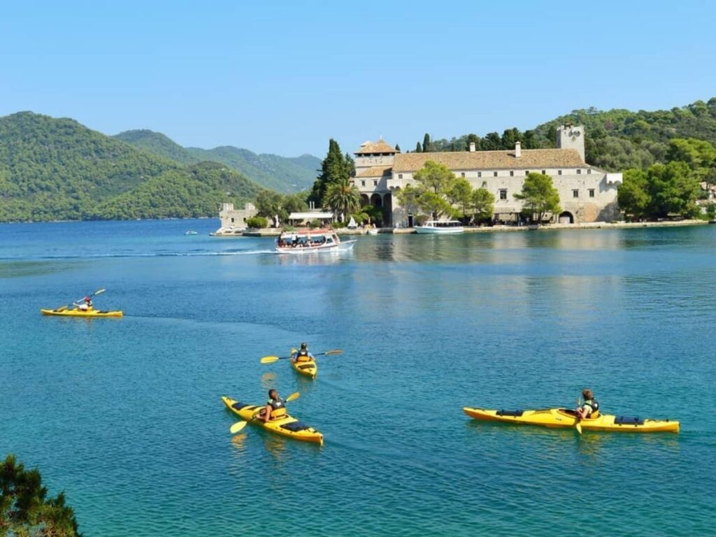 Two kayaks paddling through a narrow channel on Veliko Jezero, calm water reflecting the trees