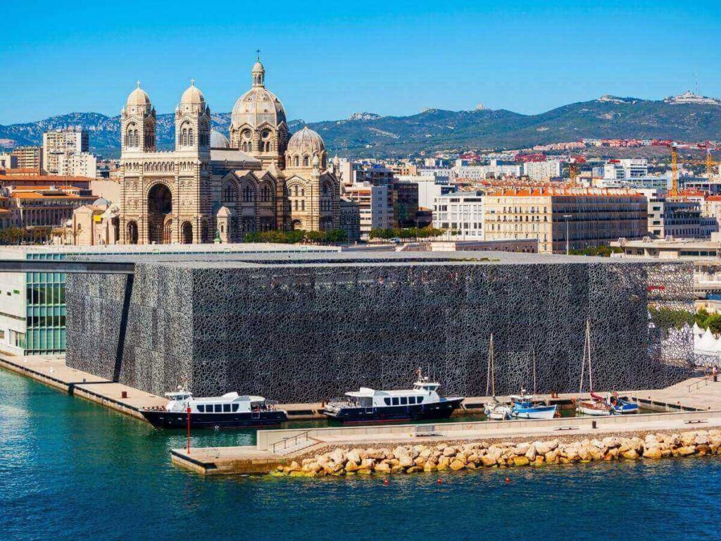 View from the MUCEM footbridge toward Fort Saint-Jean, with the sea beneath and modern lattice façade details