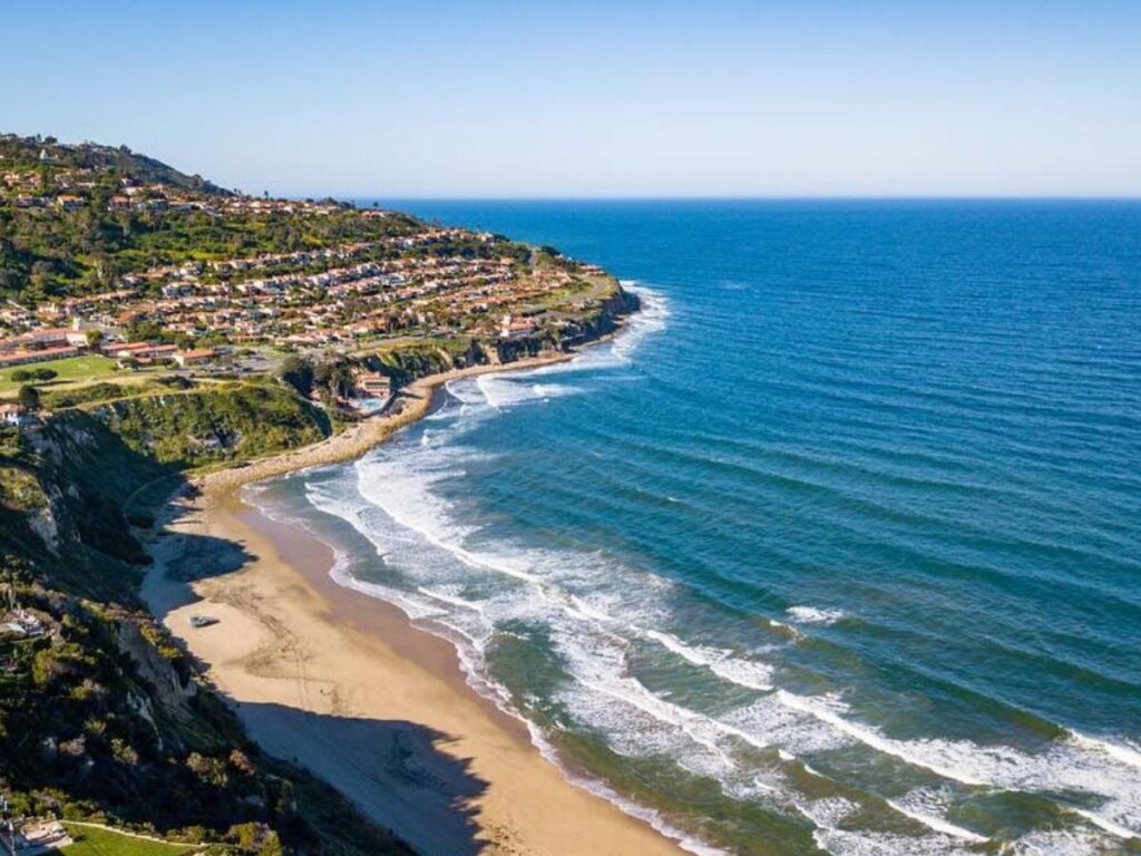 Pebbly shoreline at Rat Beach with crystal-clear turquoise water and swimmers on rocky ledges