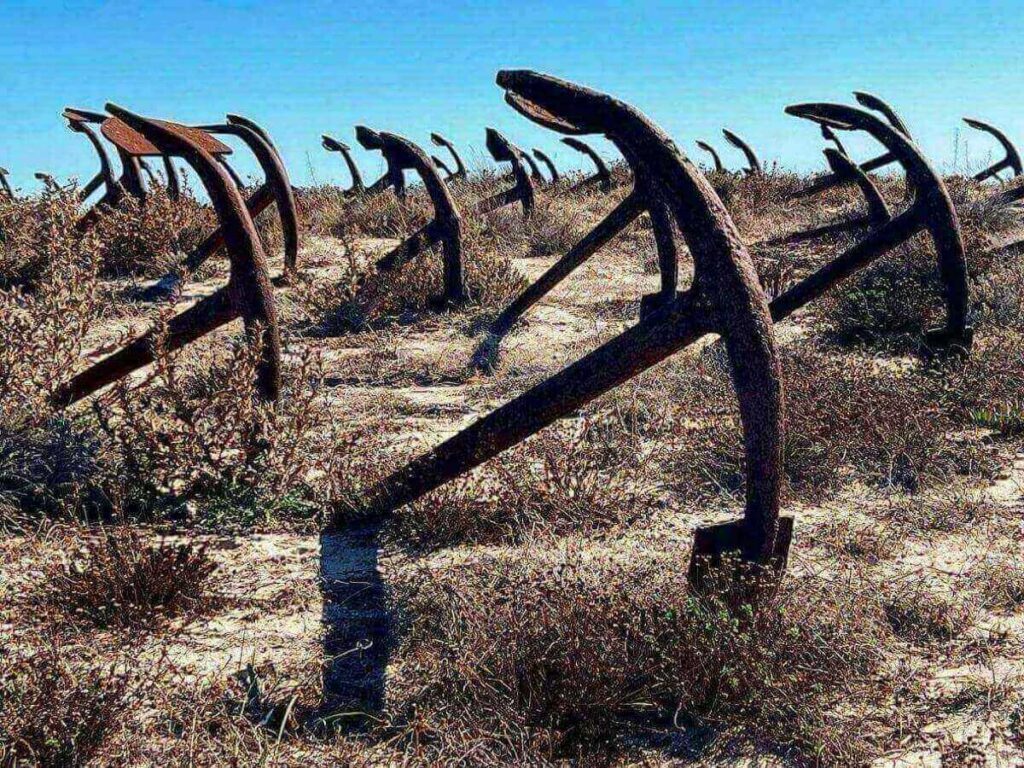 Rusted anchors of the Barril anchor cemetery on Tavira Island beach with a small train in the distance