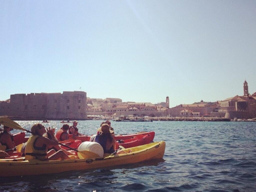 Two kayakers paddling beneath the Dubrovnik city walls at midday