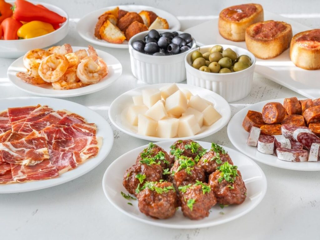 Assorted tapas on a wooden counter: jamón, croquetas, and olives