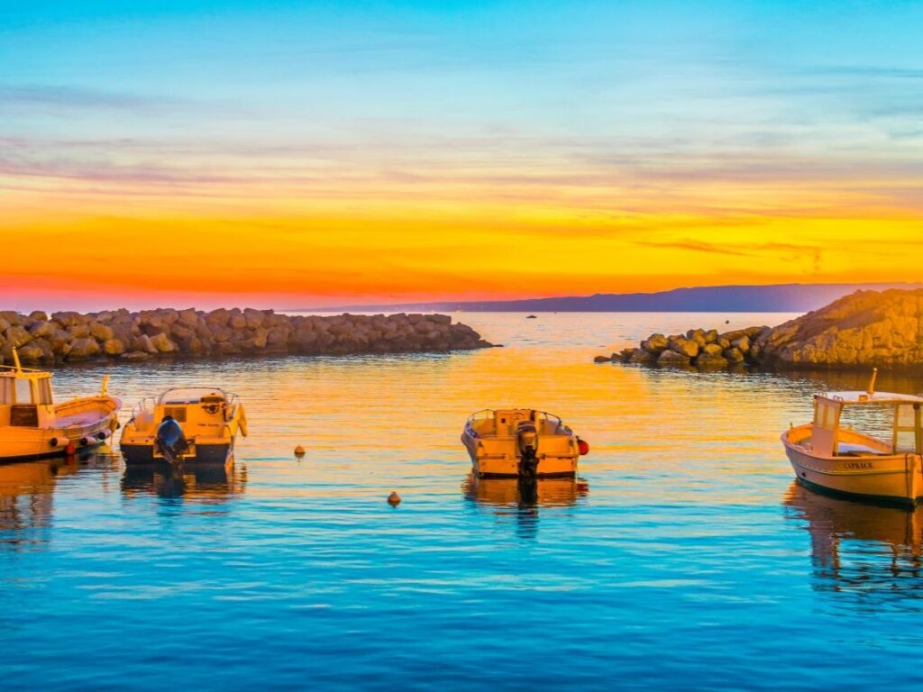 Tiny fishing boats moored in Vallon des Auffes at sunset with fishermen and waterside tables
